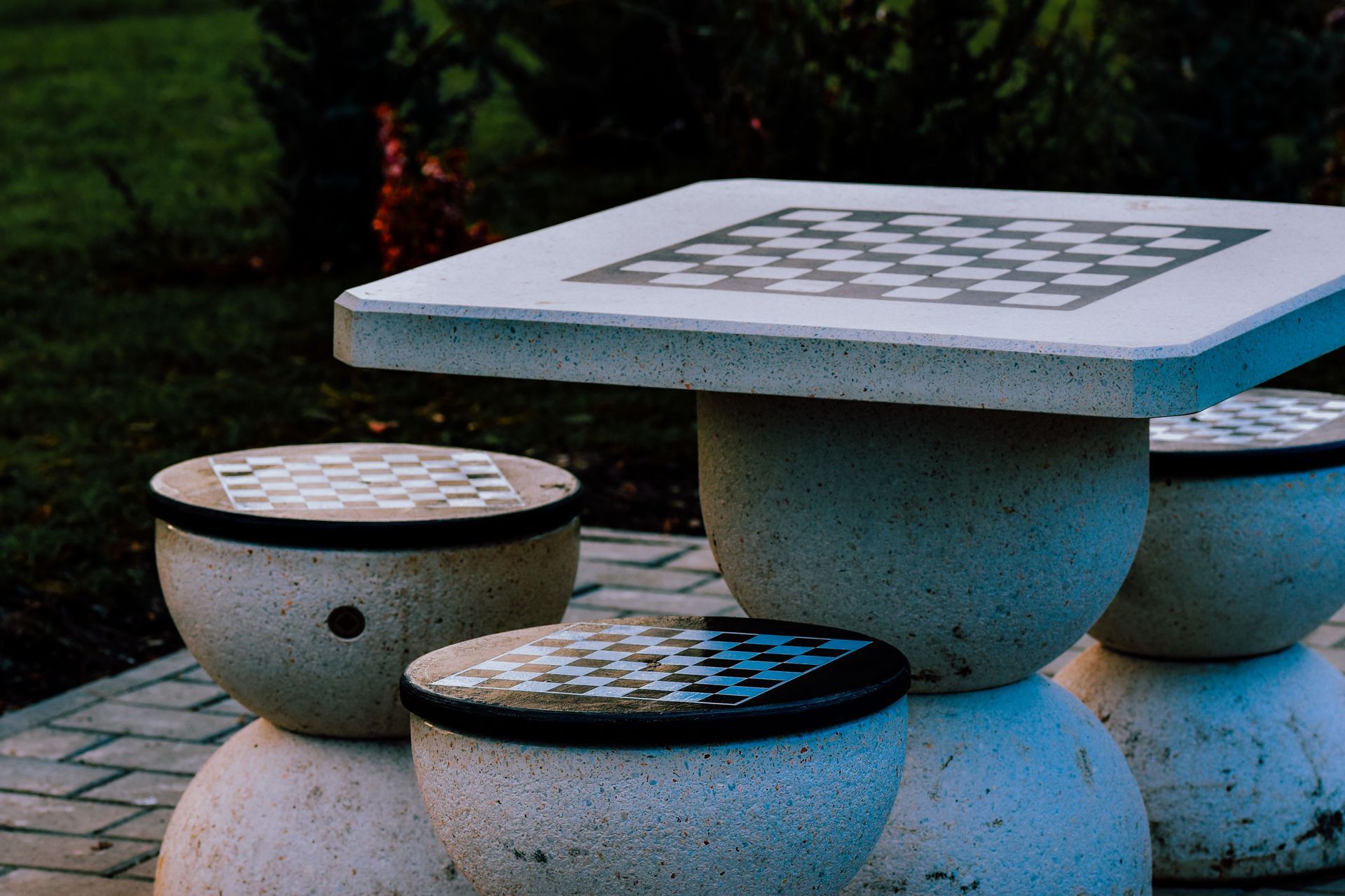Stone outdoor table and stools with checkerboard tops in a garden