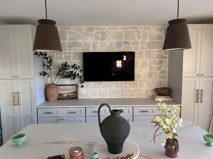 Kitchen with stone accent wall, TV, cabinetry, island with decorations, and pendant lights.