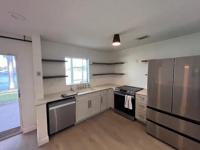 Modern kitchen with stainless steel appliances, open shelving, and light wood flooring.