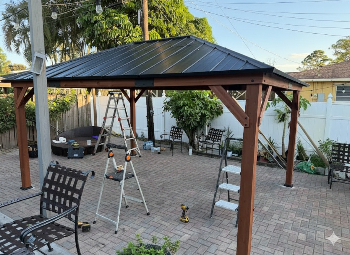 Brown wooden gazebo with black metal roof on a brick patio, surrounded by chairs and ladders.