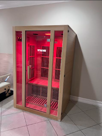 Infrared sauna with red interior glow, wooden frame, glass door, in a room with light-colored walls and tiled floor.