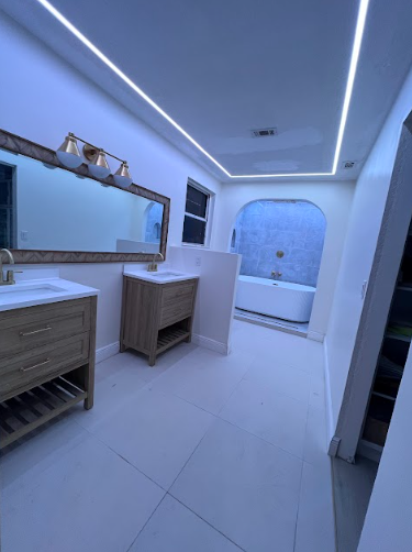 Modern bathroom with white walls, wood cabinets, large mirror, and recessed lighting.