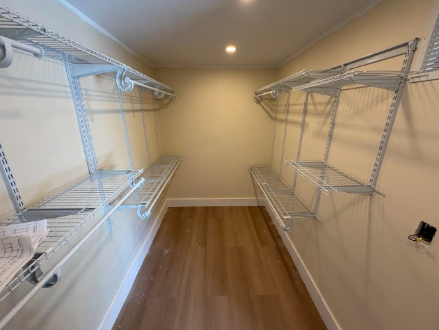 Empty walk-in closet with wire shelving and a light-colored wood floor. The walls are light beige.