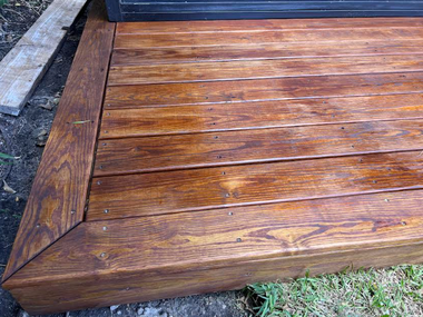 Wooden deck with stained planks, showcasing a corner detail, outdoors.