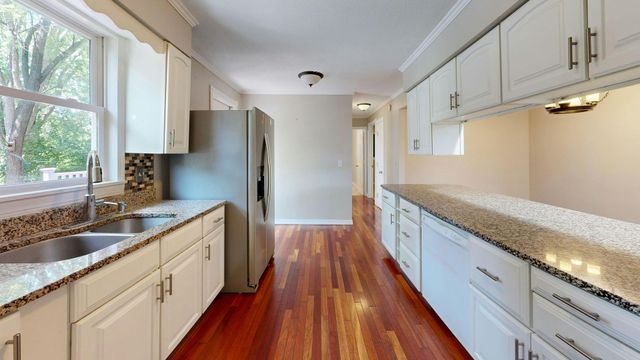 Bright kitchen with white cabinets, granite counters, stainless steel fridge, and wood floors.