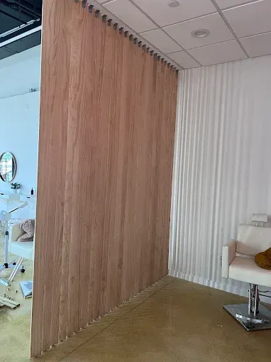 Wooden wall partition separates a salon area with white curtains and a white chair.