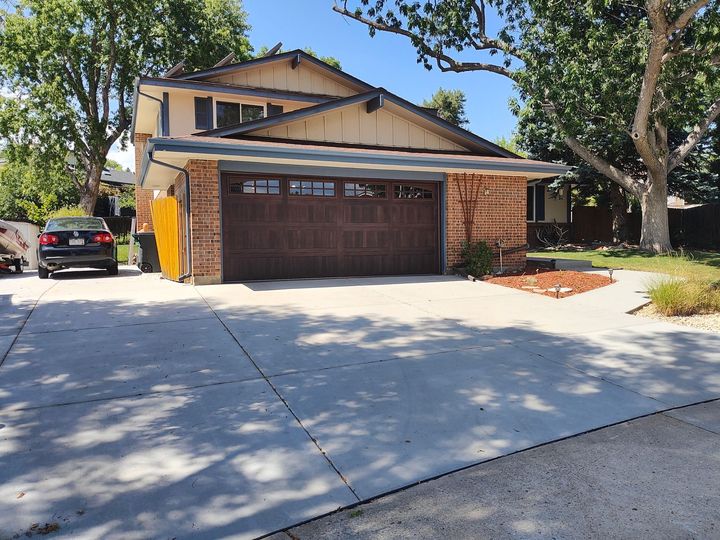Suburban two-story house with a brown garage door, driveway, and trees in front