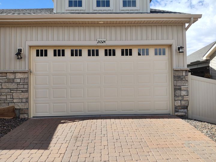 Beige garage door with driveway and stone wall under bright sunlight