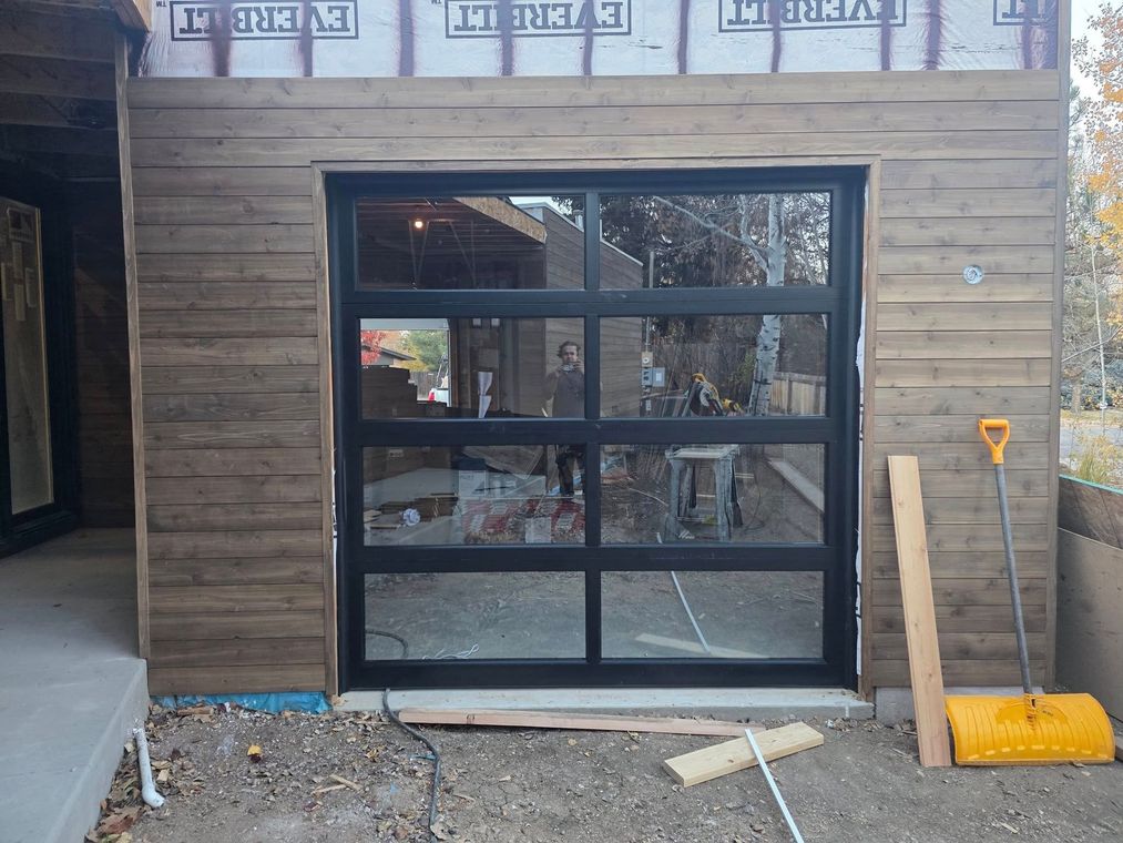 Wood-paneled garage front with a black-framed glass roll-up door and a yellow shovel leaning nearby