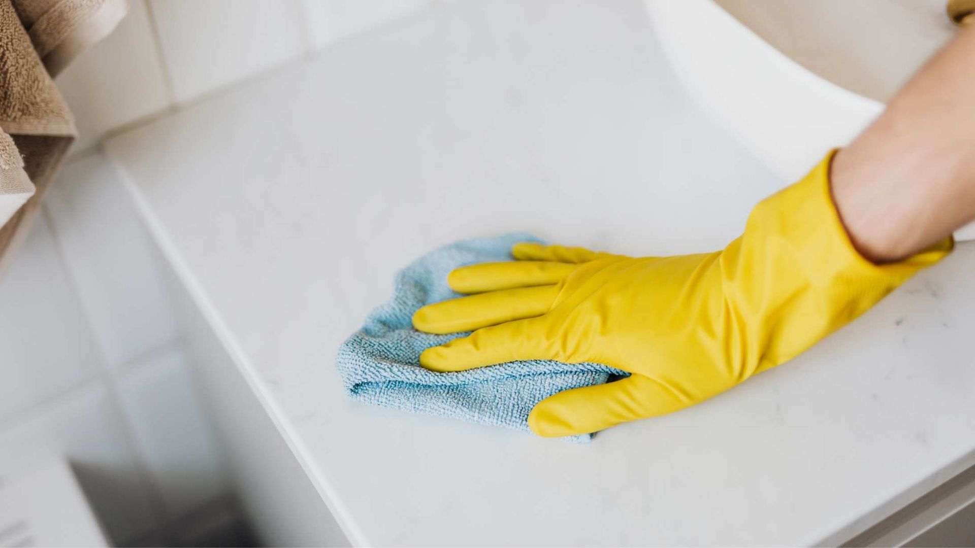 A gloved hand wipes a white surface with a blue cloth.