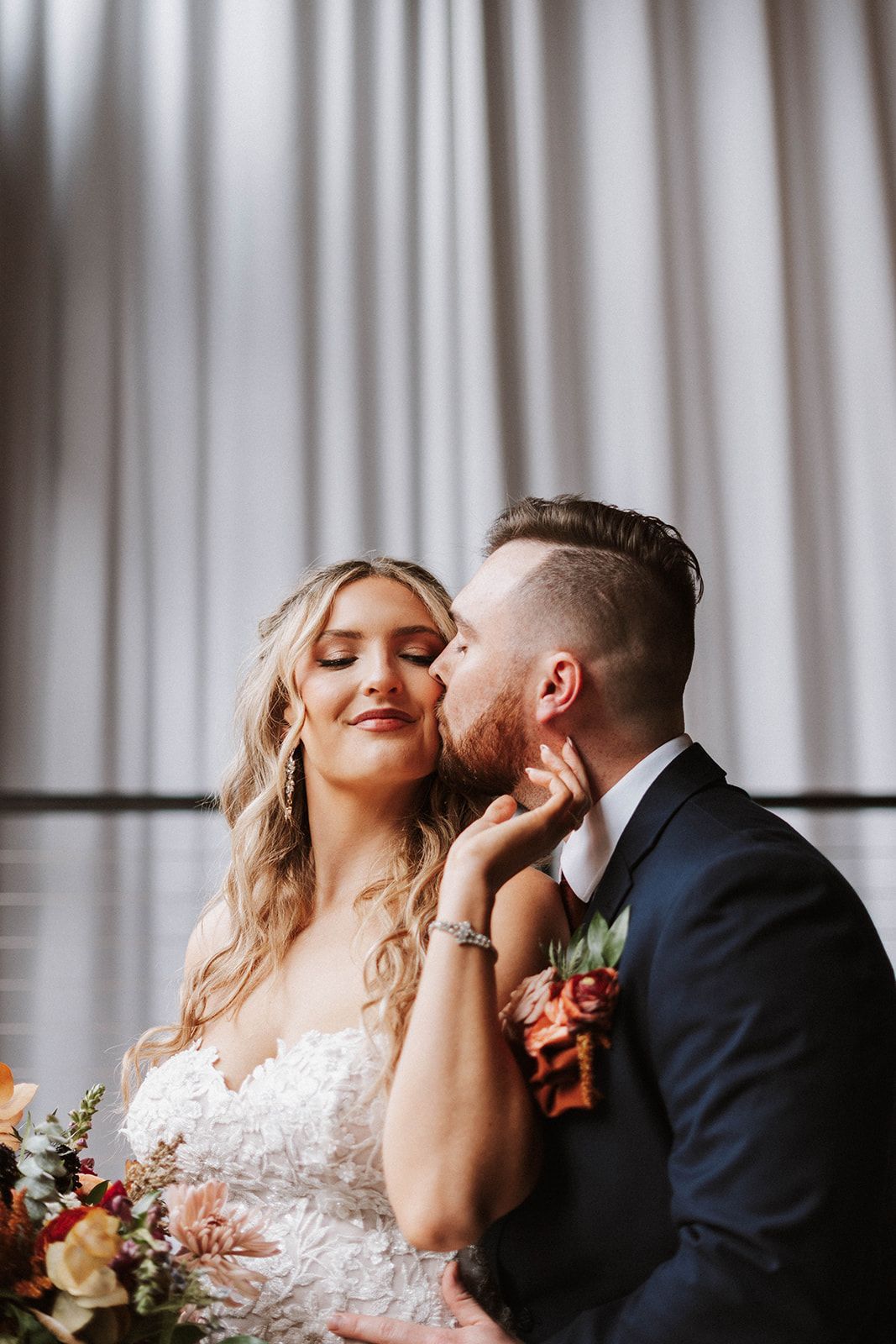 A bride and groom are kissing in front of a white curtain.