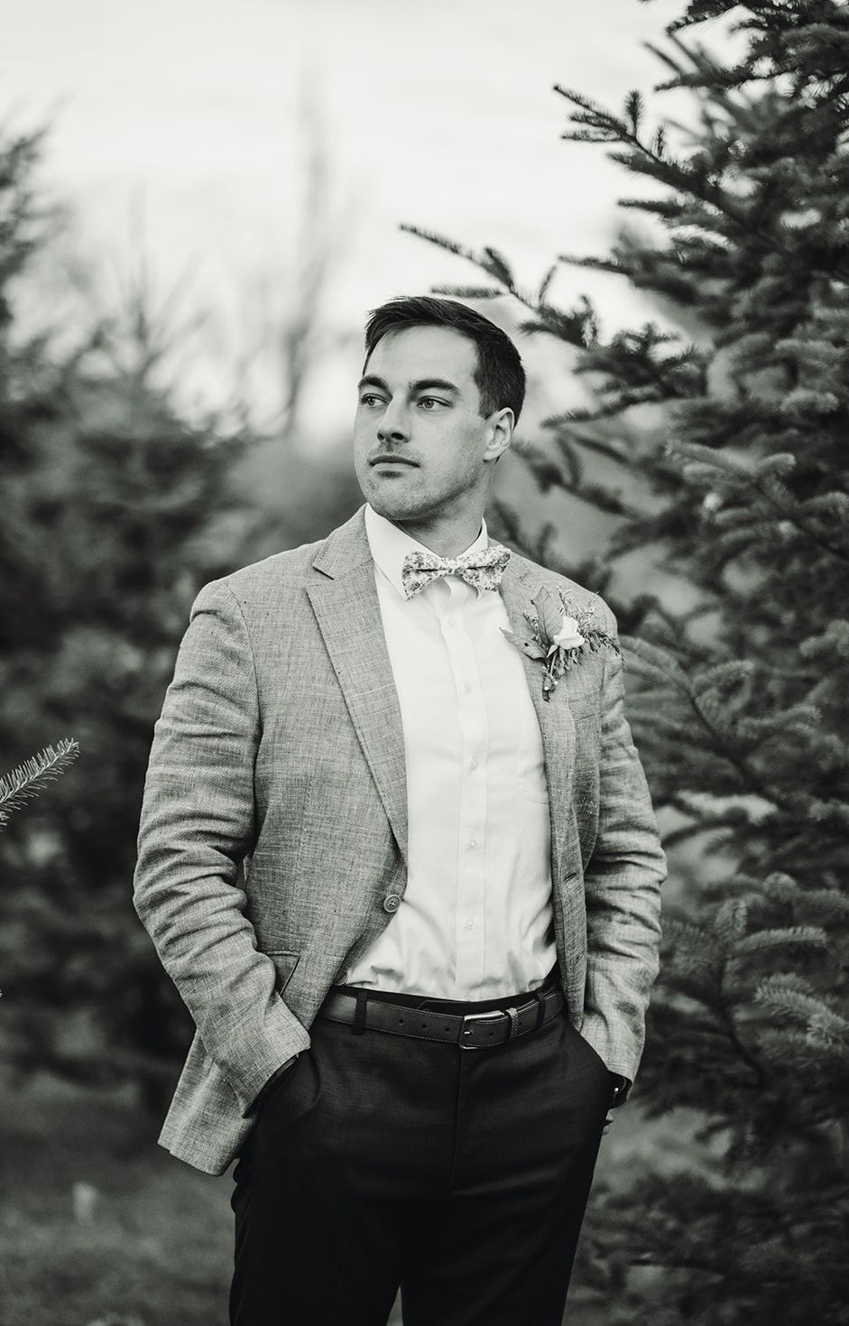 A man in a suit and bow tie is standing in front of a christmas tree.