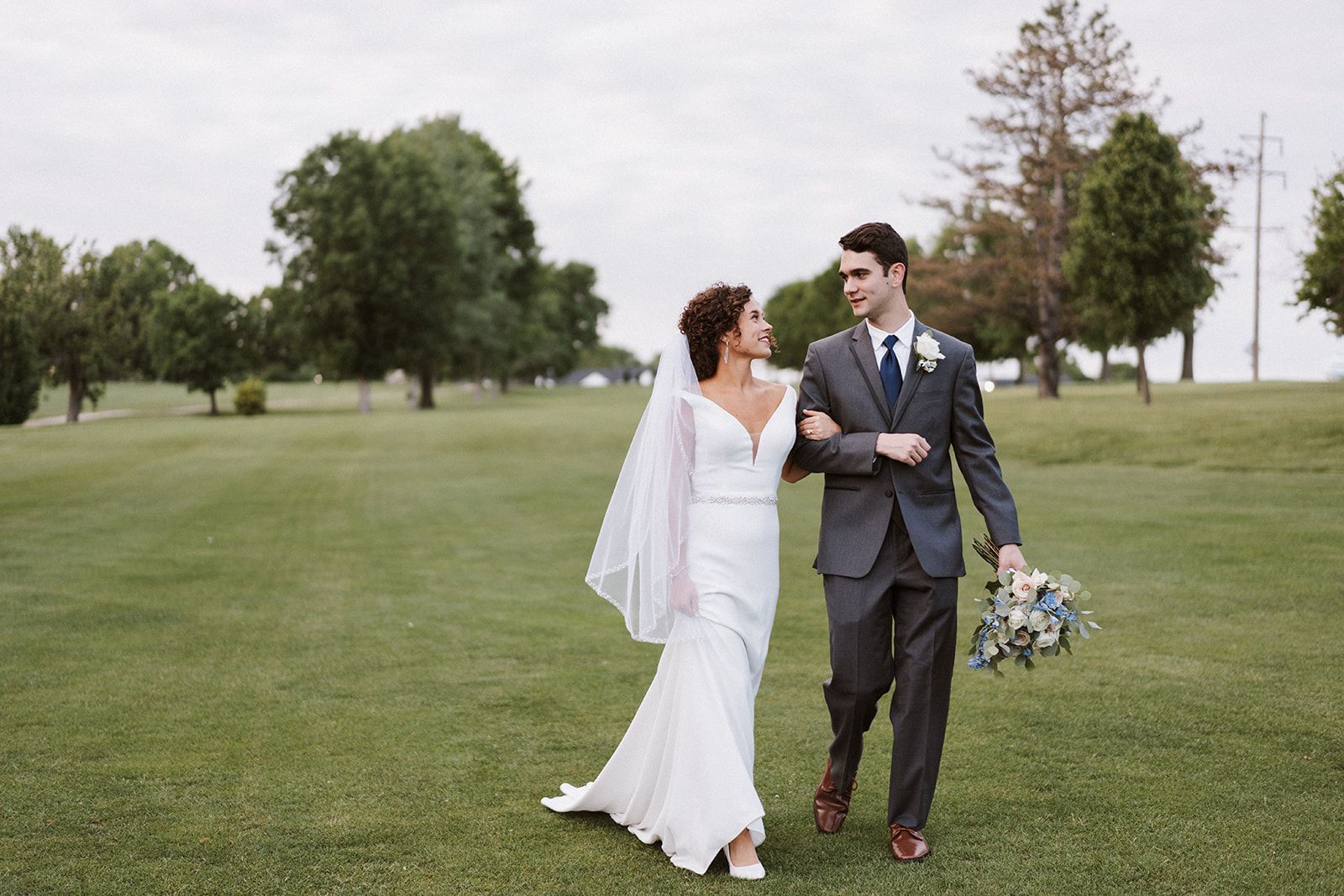 A bride and groom are walking through a grassy field.