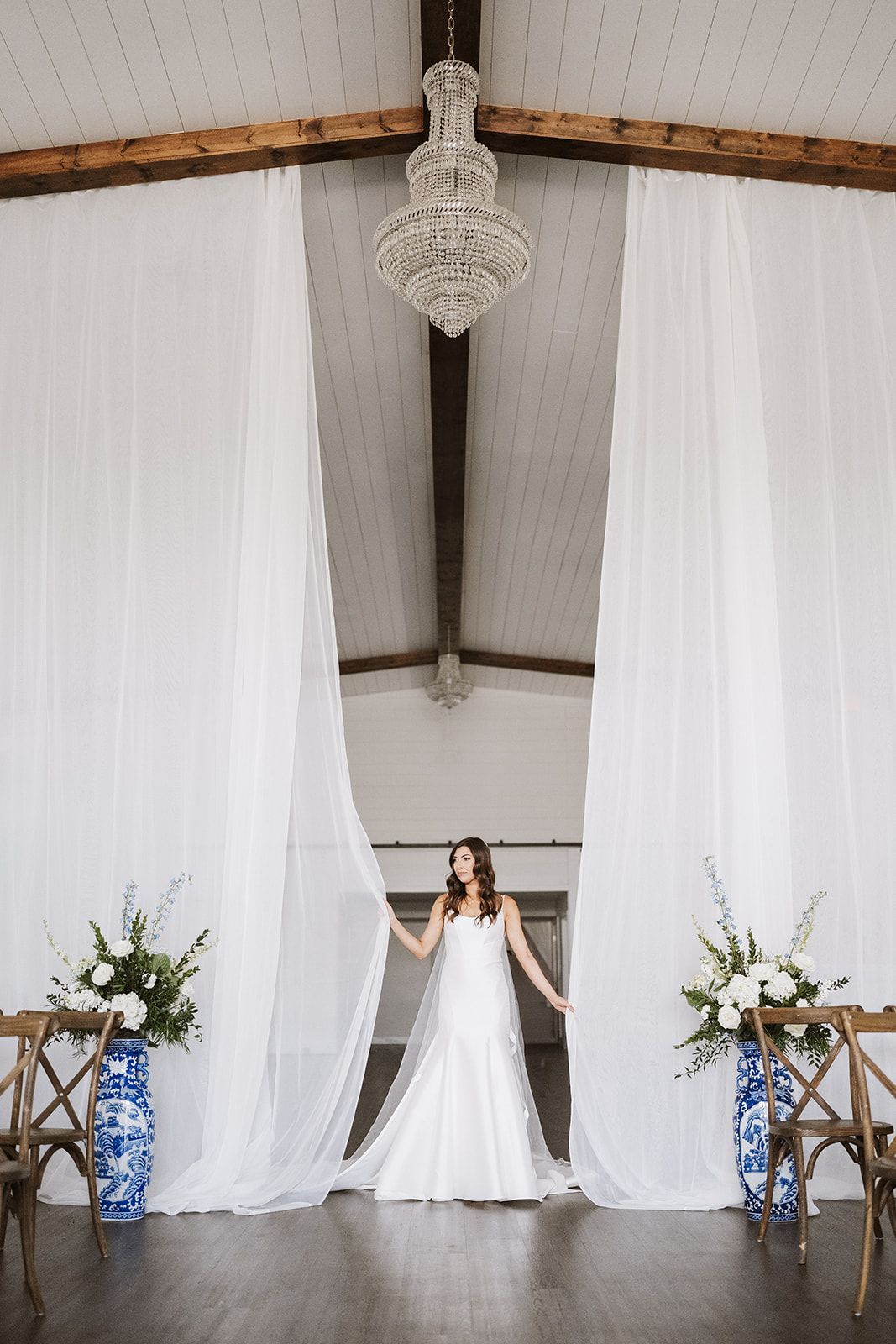 A bride in a wedding dress is standing in front of a white chandelier.