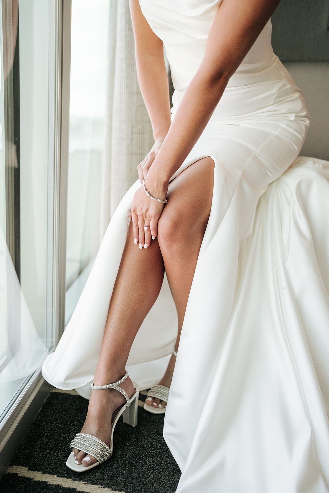 A woman in a white dress is sitting on a bed with her legs crossed.