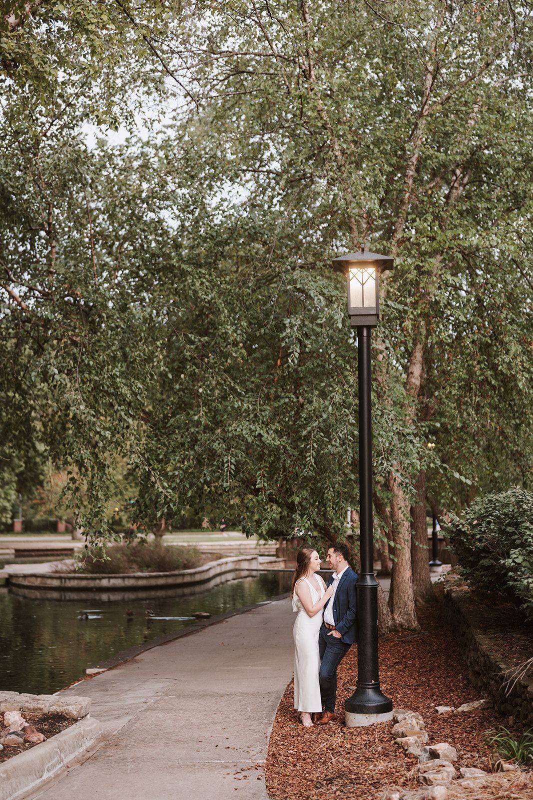 A bride and groom are standing next to a lamp post in a park.