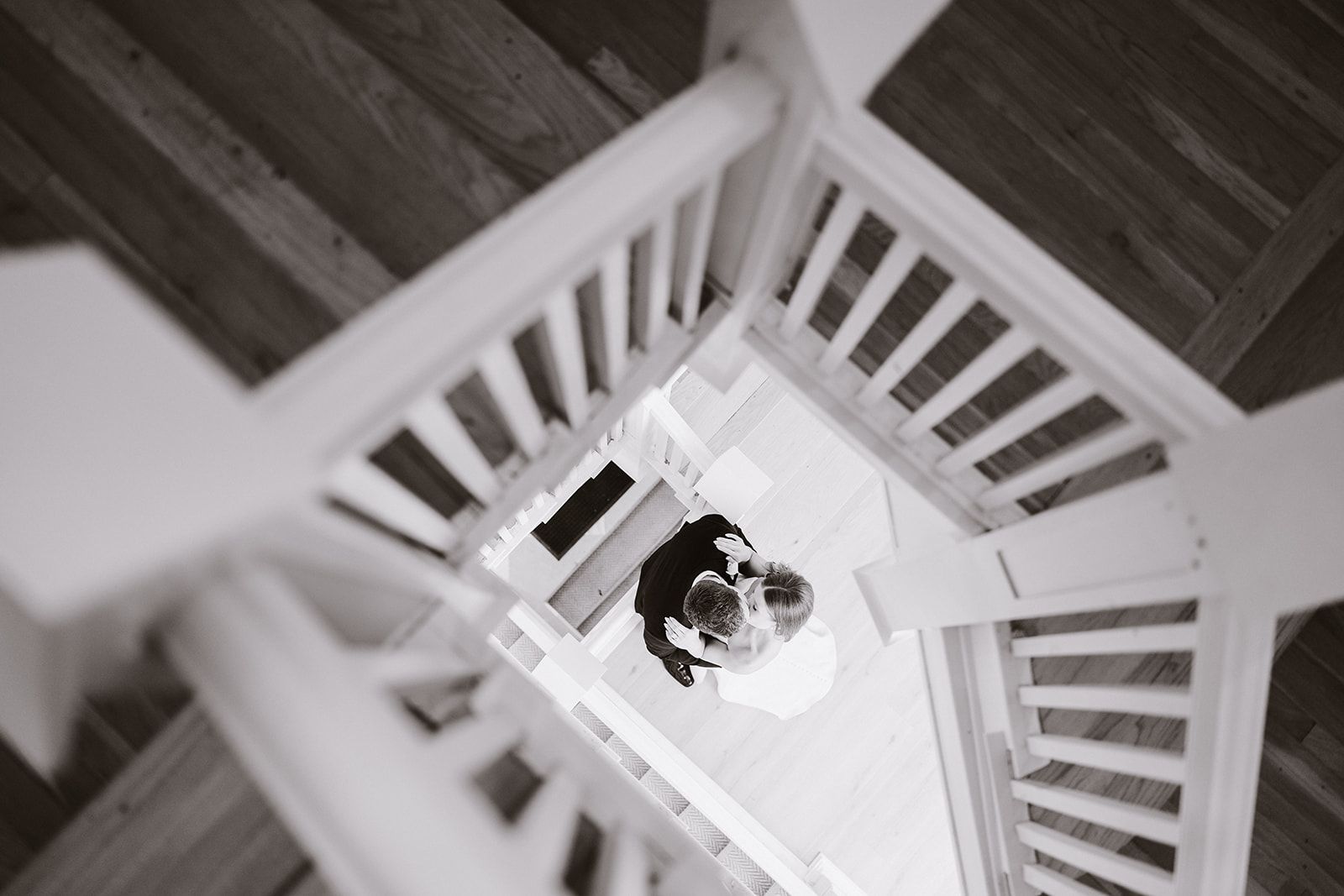 A black and white photo of a bride and groom walking down a spiral staircase.