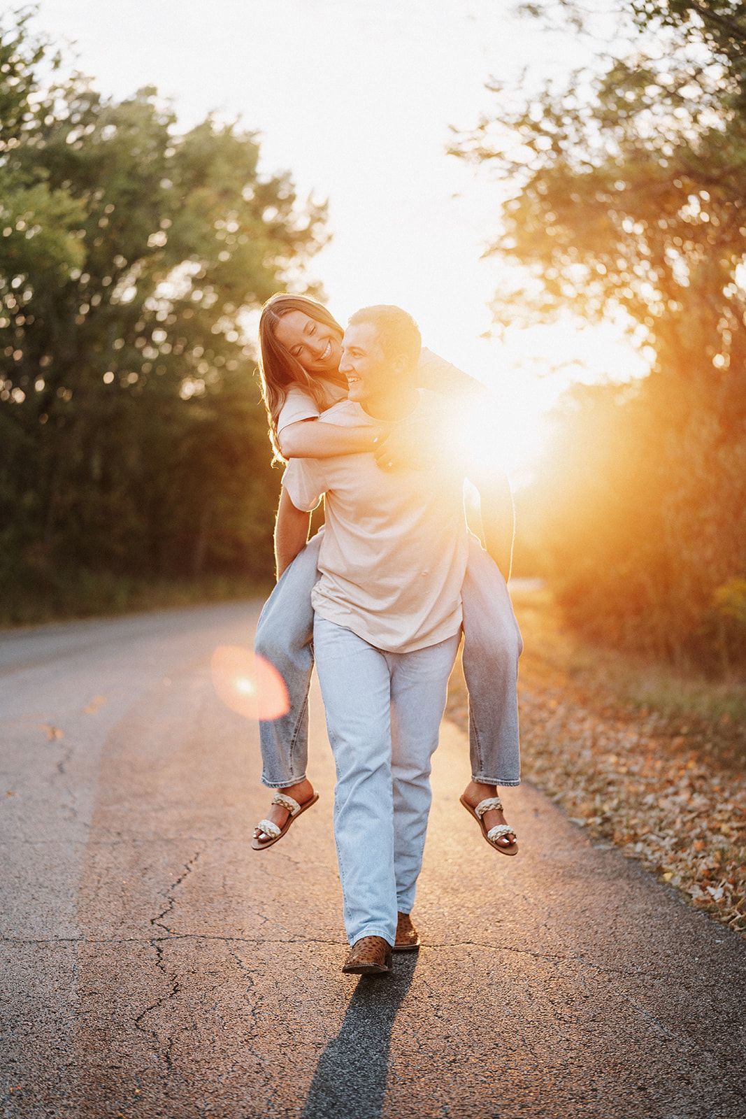 A man is carrying a woman on his shoulders down a road at sunset.