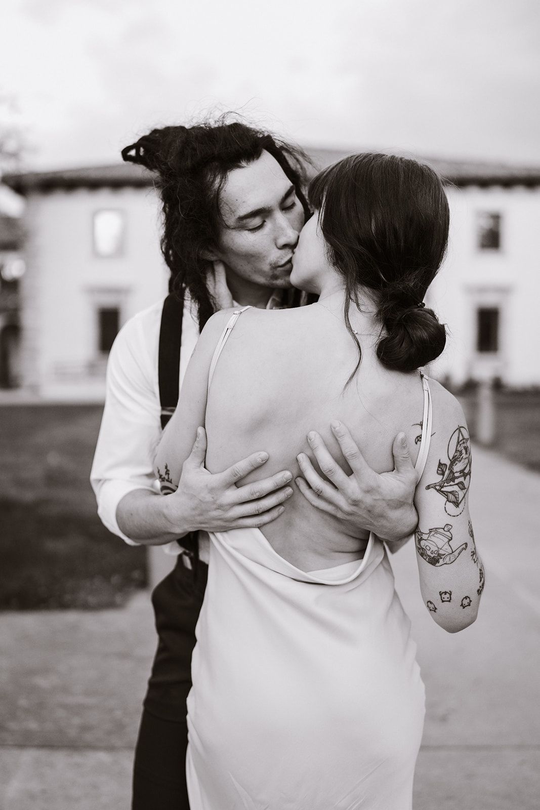 A bride and groom are kissing in front of a building in a black and white photo.