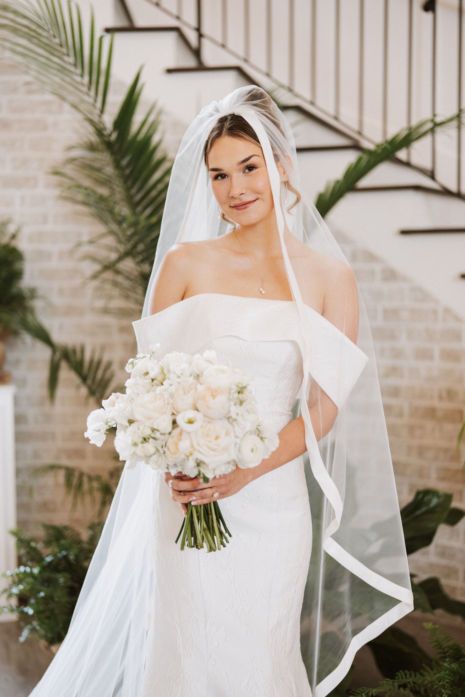 A bride in a white dress and veil is holding a bouquet of white flowers.