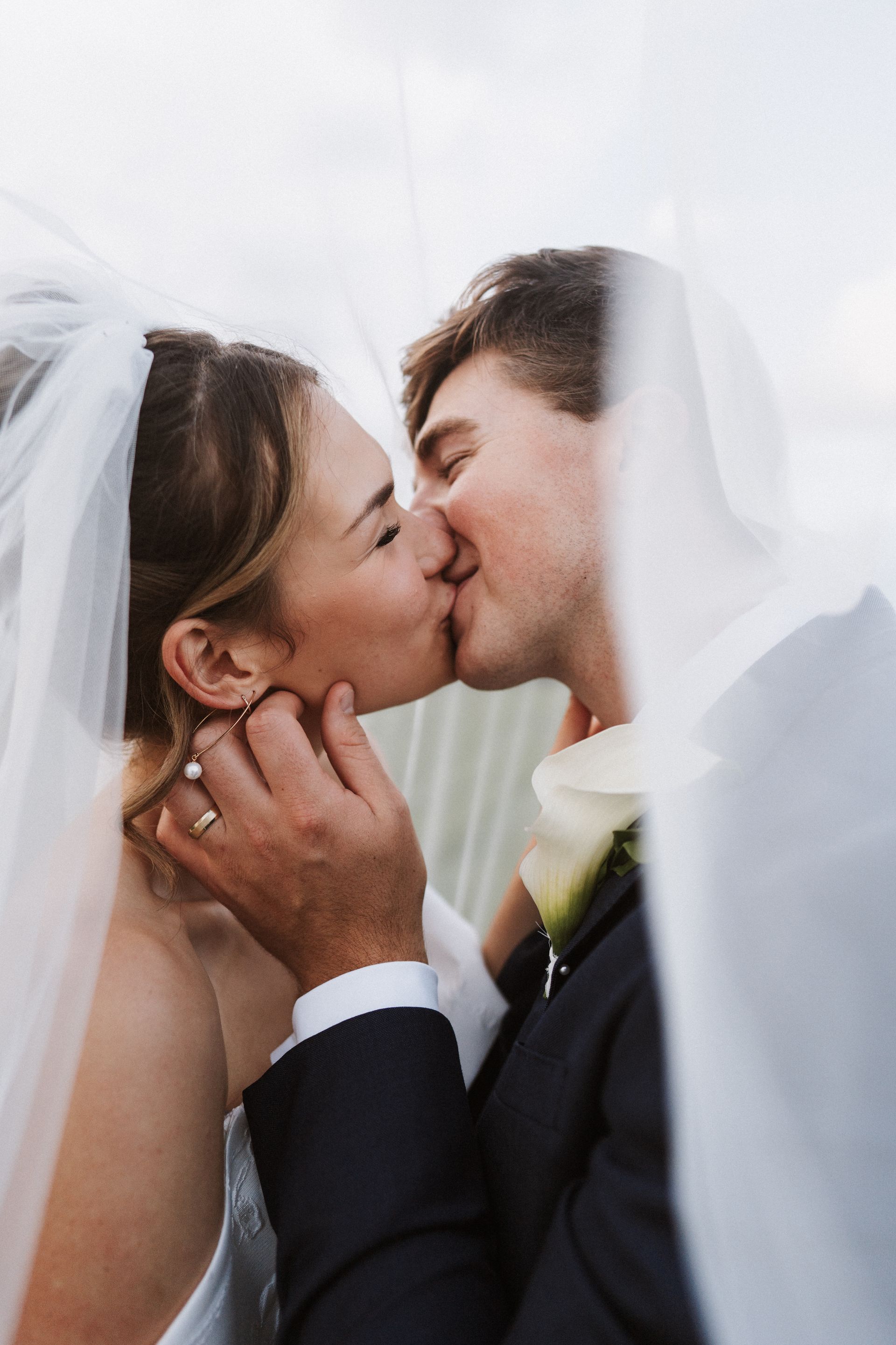 A bride and groom are kissing under a veil.
