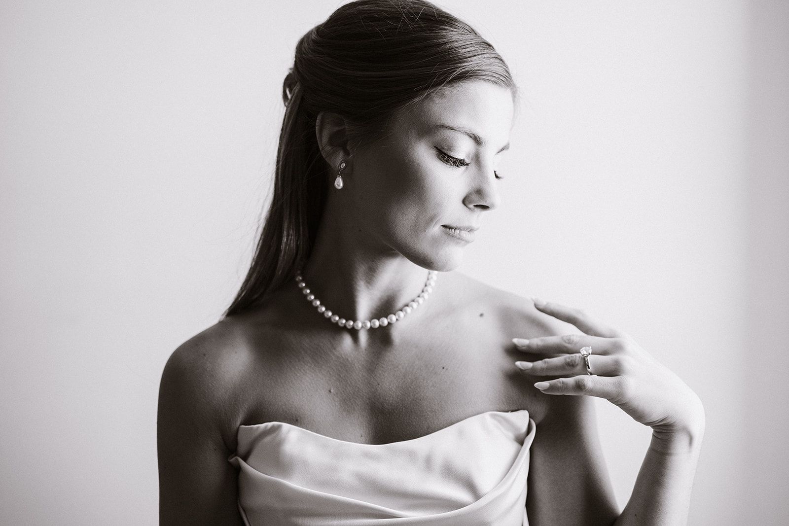 A black and white photo of a woman in a wedding dress and pearl necklace.