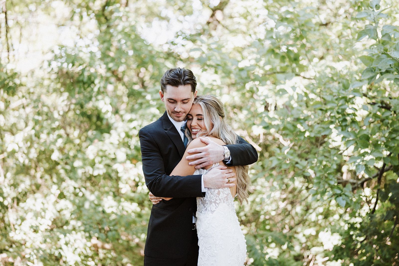 A bride and groom are hugging each other in the woods.