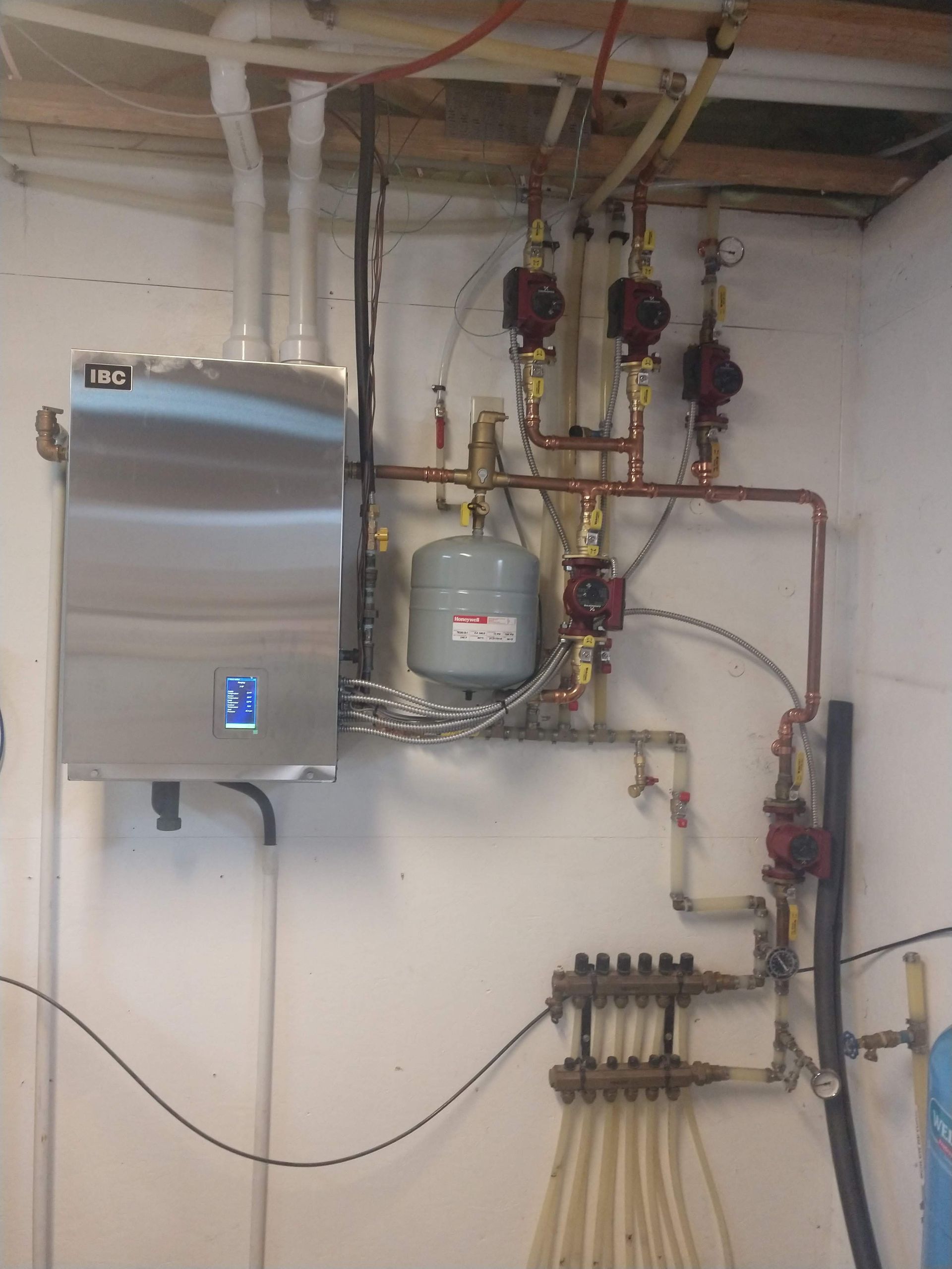 A wall-mounted boiler system with pipes, red pumps, and a grey expansion tank in a utility area.