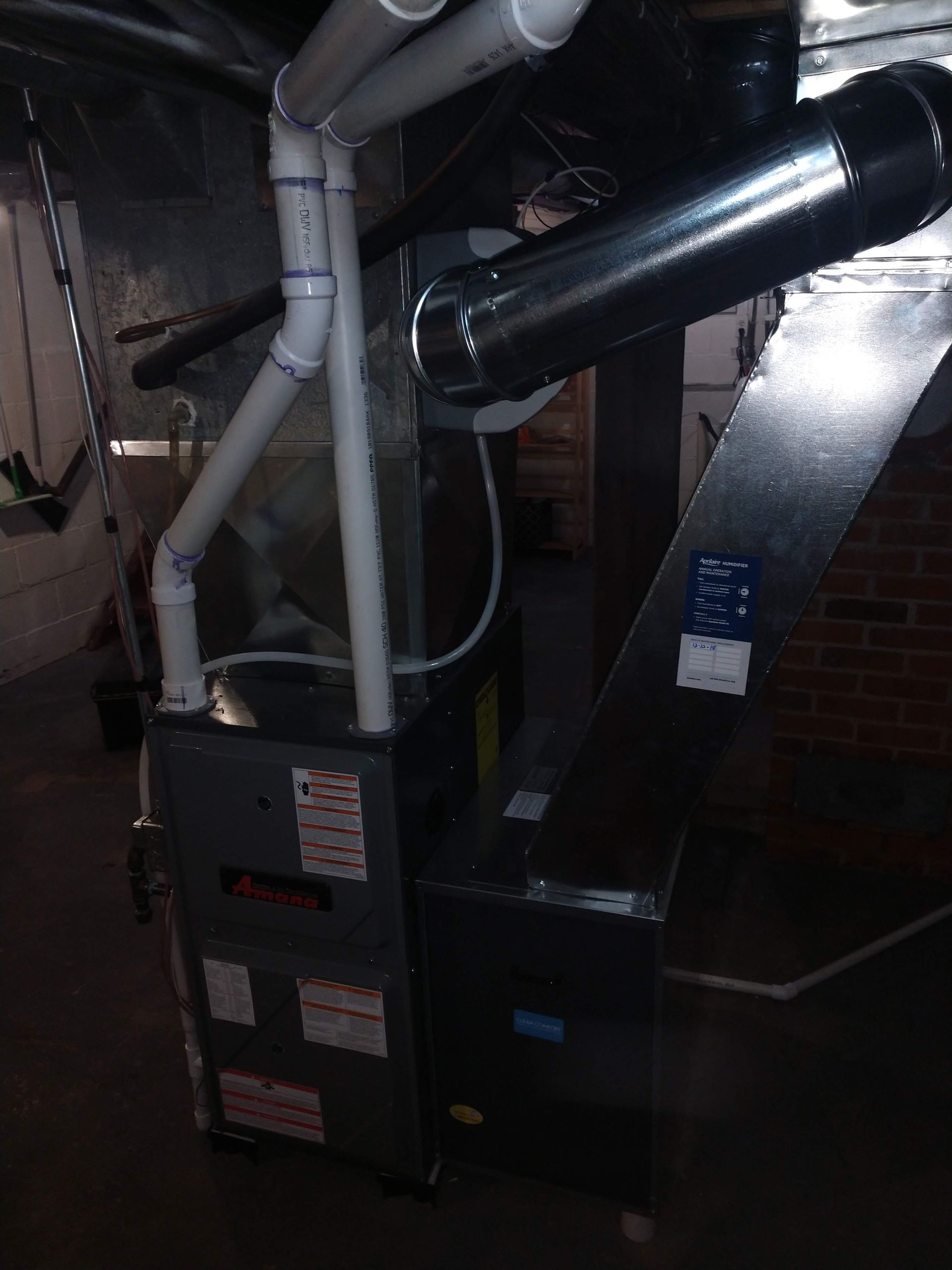 High-efficiency furnace with white PVC intake and exhaust pipes and metal ductwork installed in a basement.