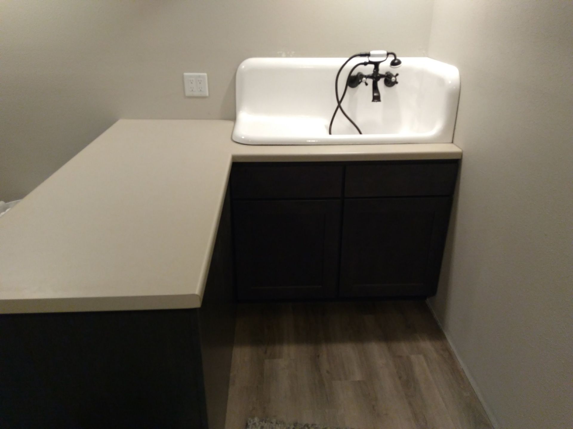 A high-backed white utility sink with a black faucet on dark cabinets next to a light-colored countertop.