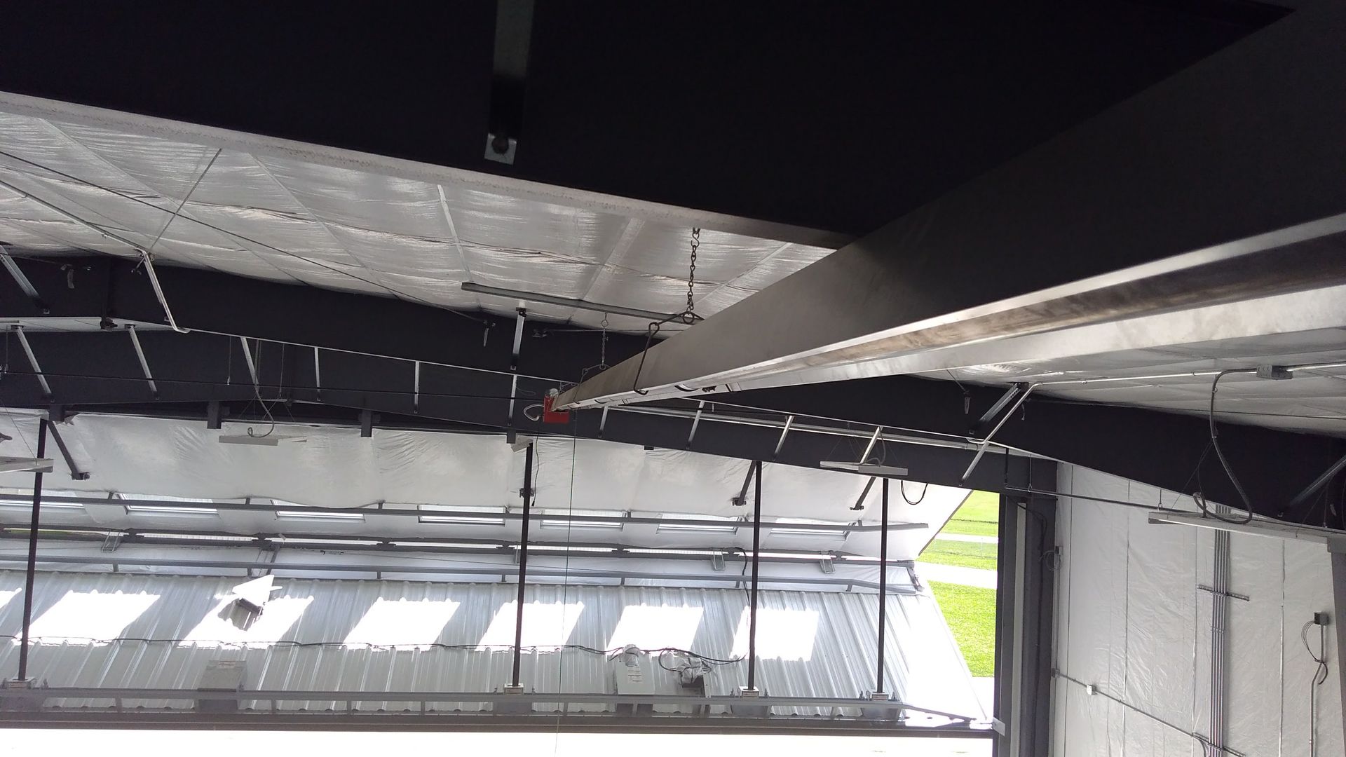 A low-angle view of a building interior featuring exposed black steel beams, metal ceiling panels, and a large window.