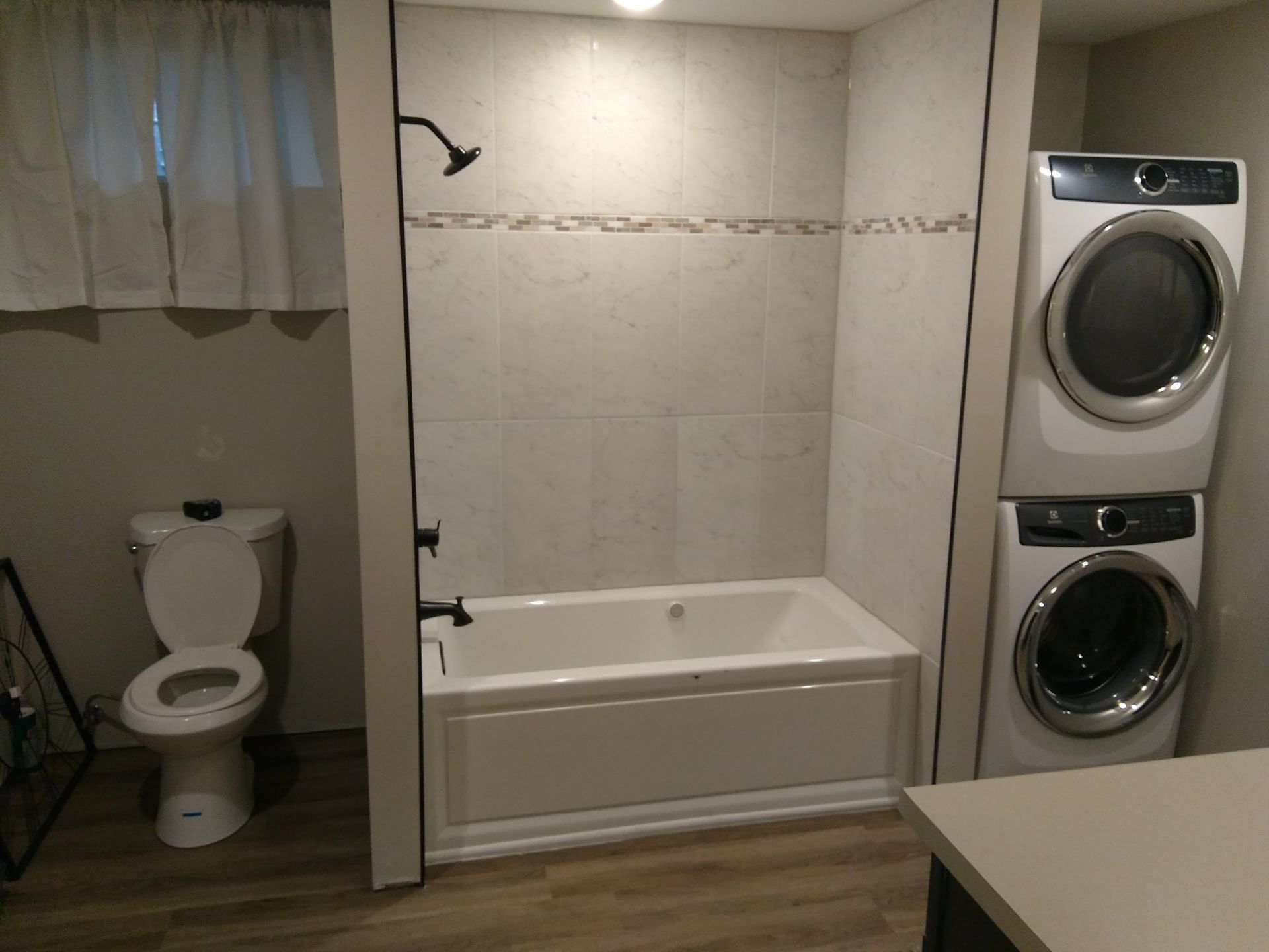 A bathroom containing a toilet, a bathtub with a shower head, and a stacked washer and dryer unit.