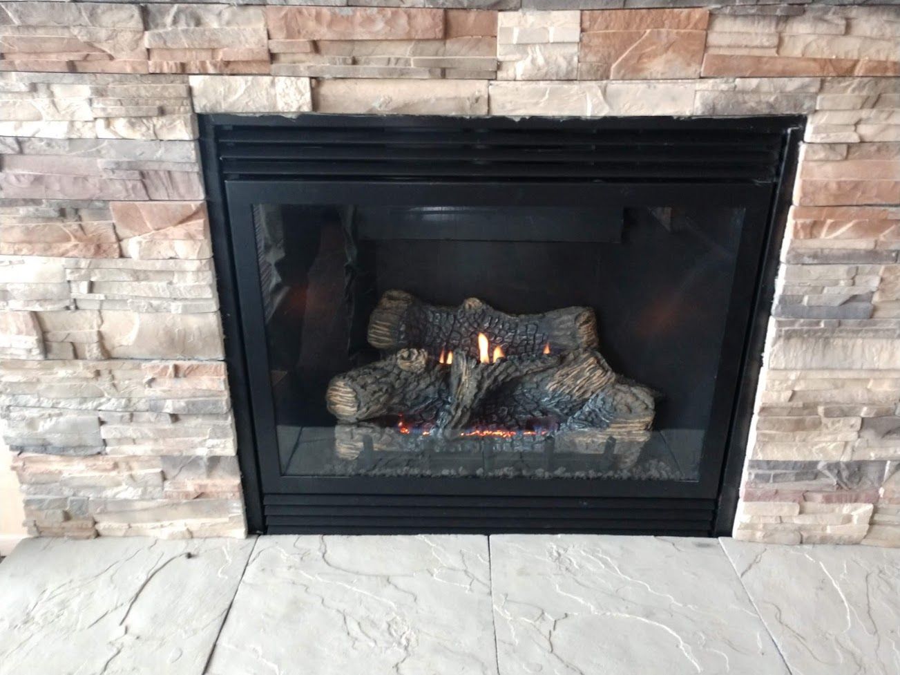 A gas fireplace with glowing logs set into a textured, multi-colored stone wall above a gray stone hearth.
