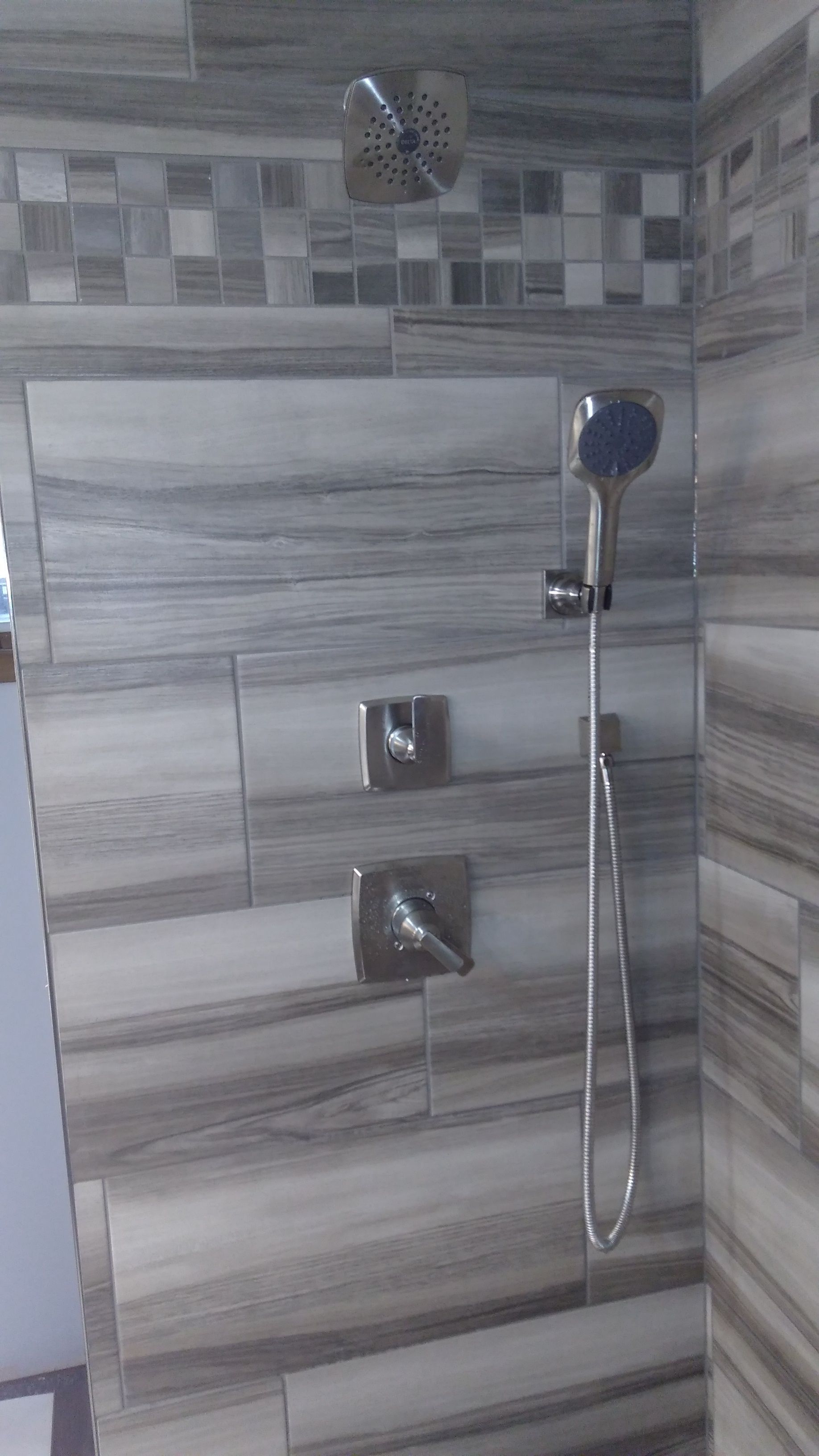 A walk-in shower with horizontal gray wood-look tiles, a mosaic accent strip, a rainfall showerhead, and a hand shower.