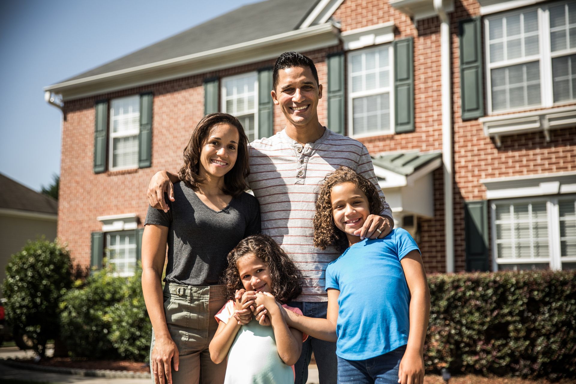 Happy family standing outside their home, confidently covered by homeowner’s insurance.
