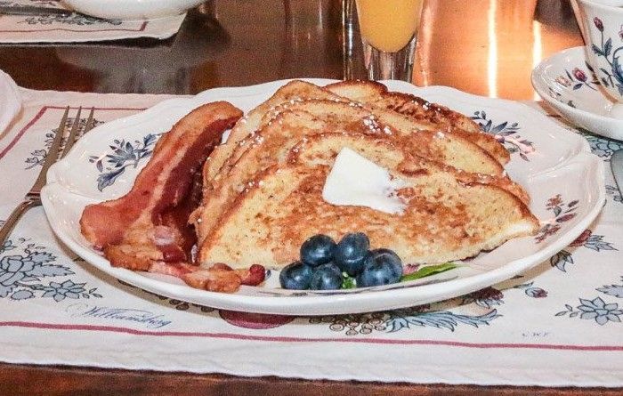 A plate of french toast with bacon and blueberries on a table.