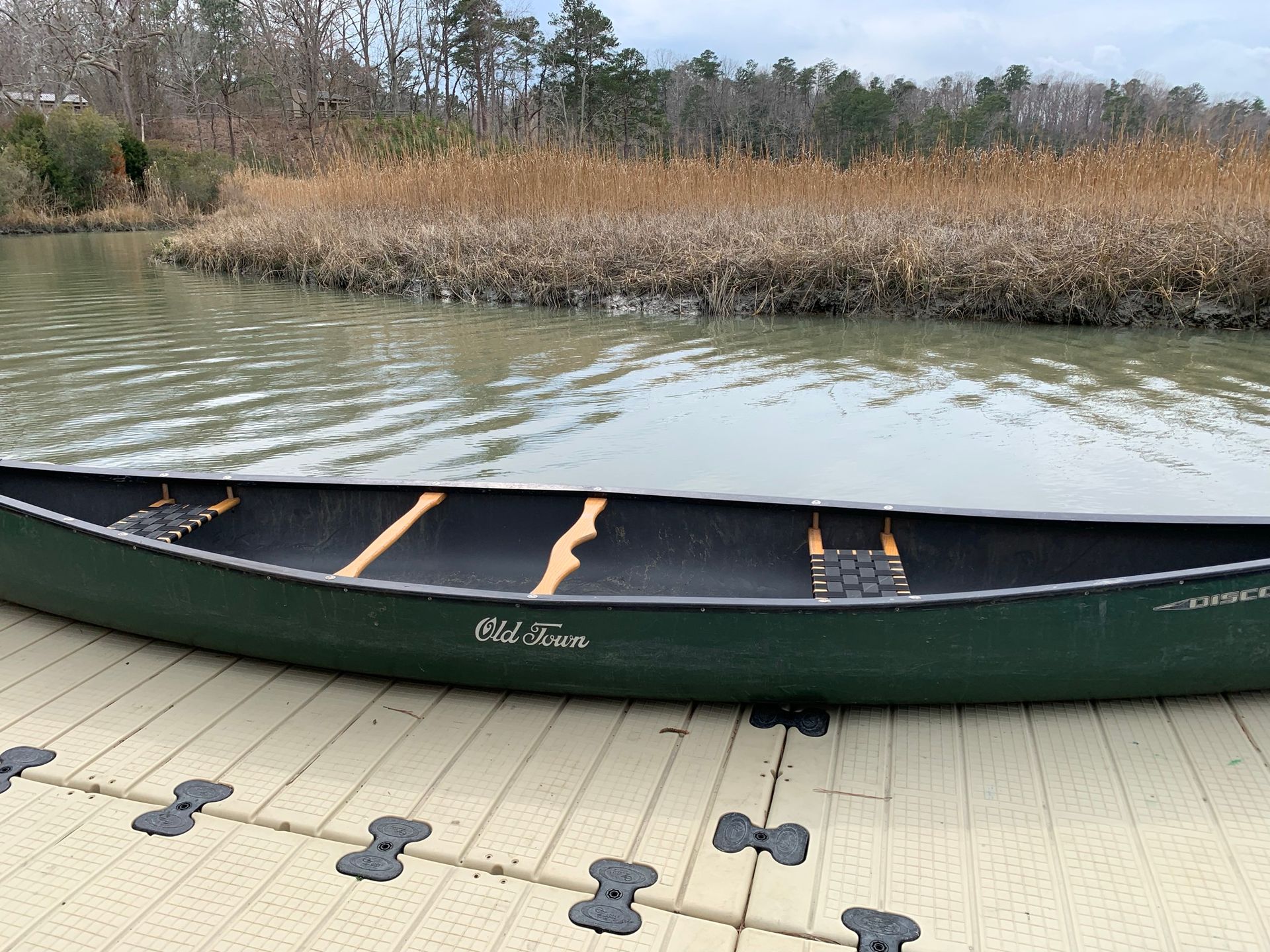 A green canoe is sitting on a dock next to a body of water.