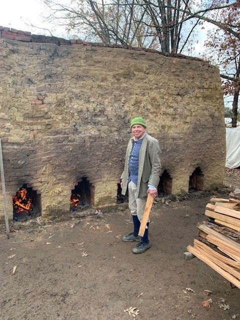A man in a green hat is standing in front of a brick wall holding a wooden stick.