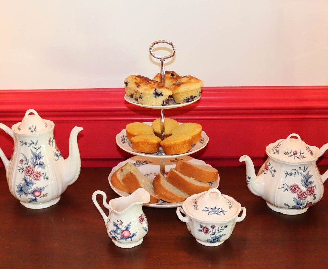 A set of teapots and cups with a cake stand in the background