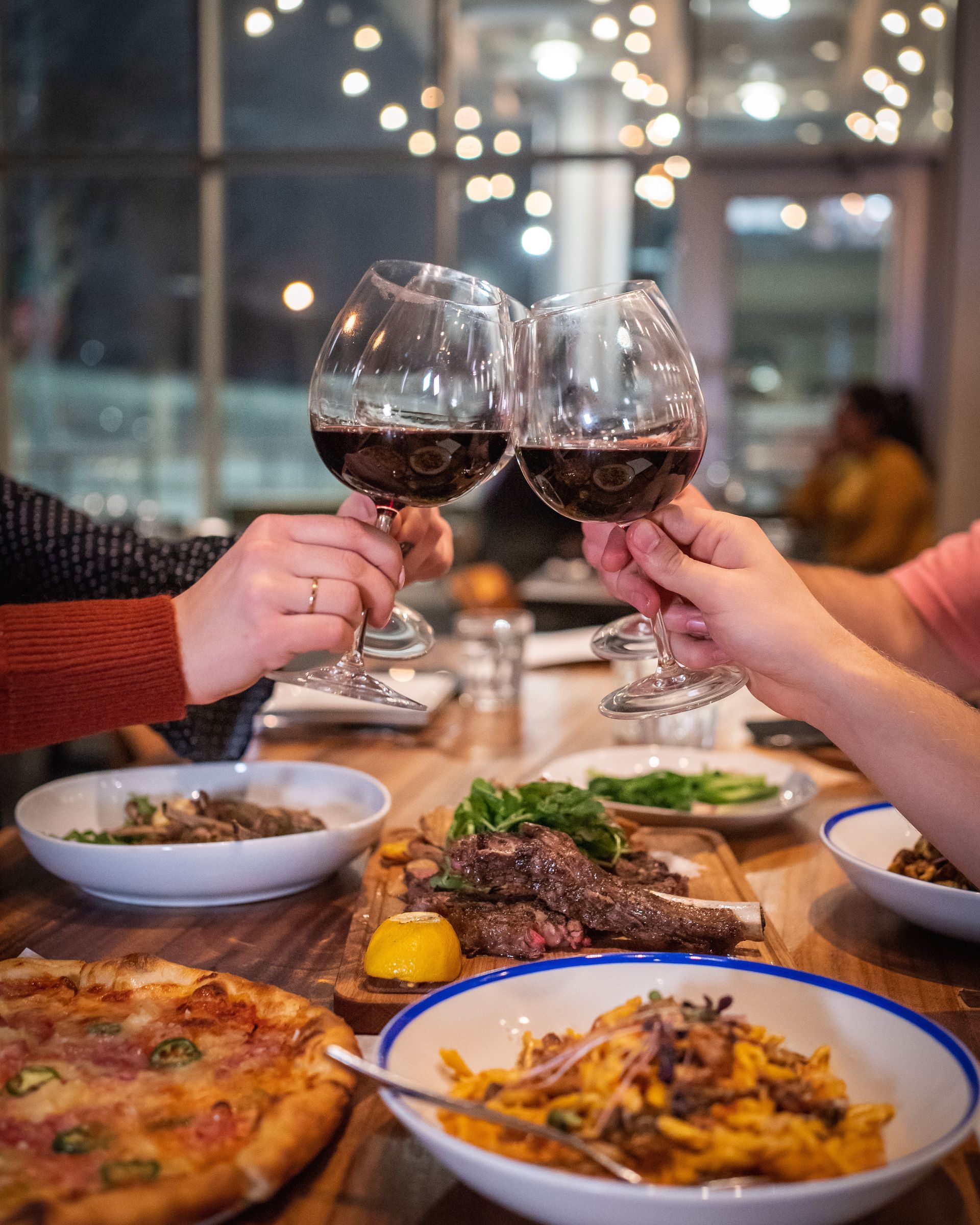 A group of people are toasting with wine glasses while sitting at a table with food.