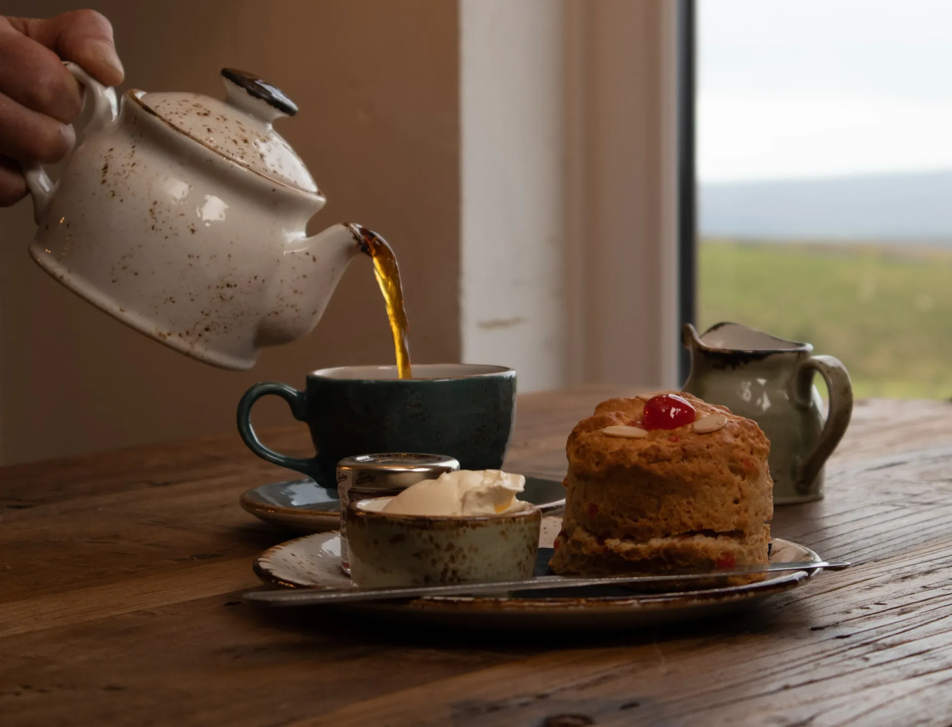 A person is pouring tea into a cup on a wooden table.