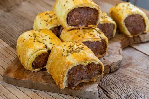 Sausage rolls are stacked on top of each other on a wooden cutting board.