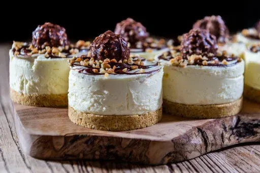 A wooden cutting board topped with a row of mini cheesecakes.