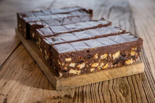 A wooden cutting board topped with slices of chocolate cake on a wooden table.