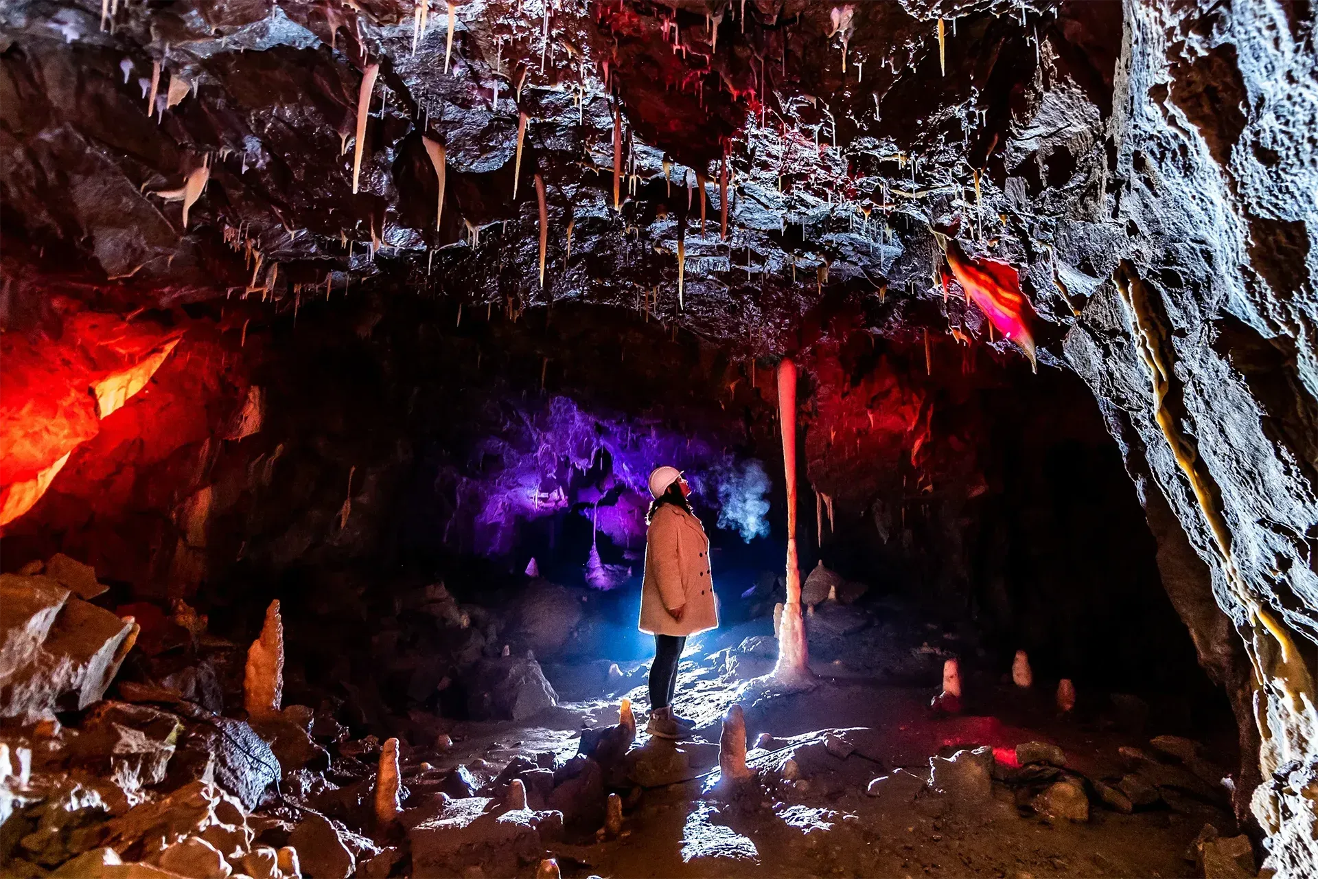A person is standing in a cave with purple and red lights.