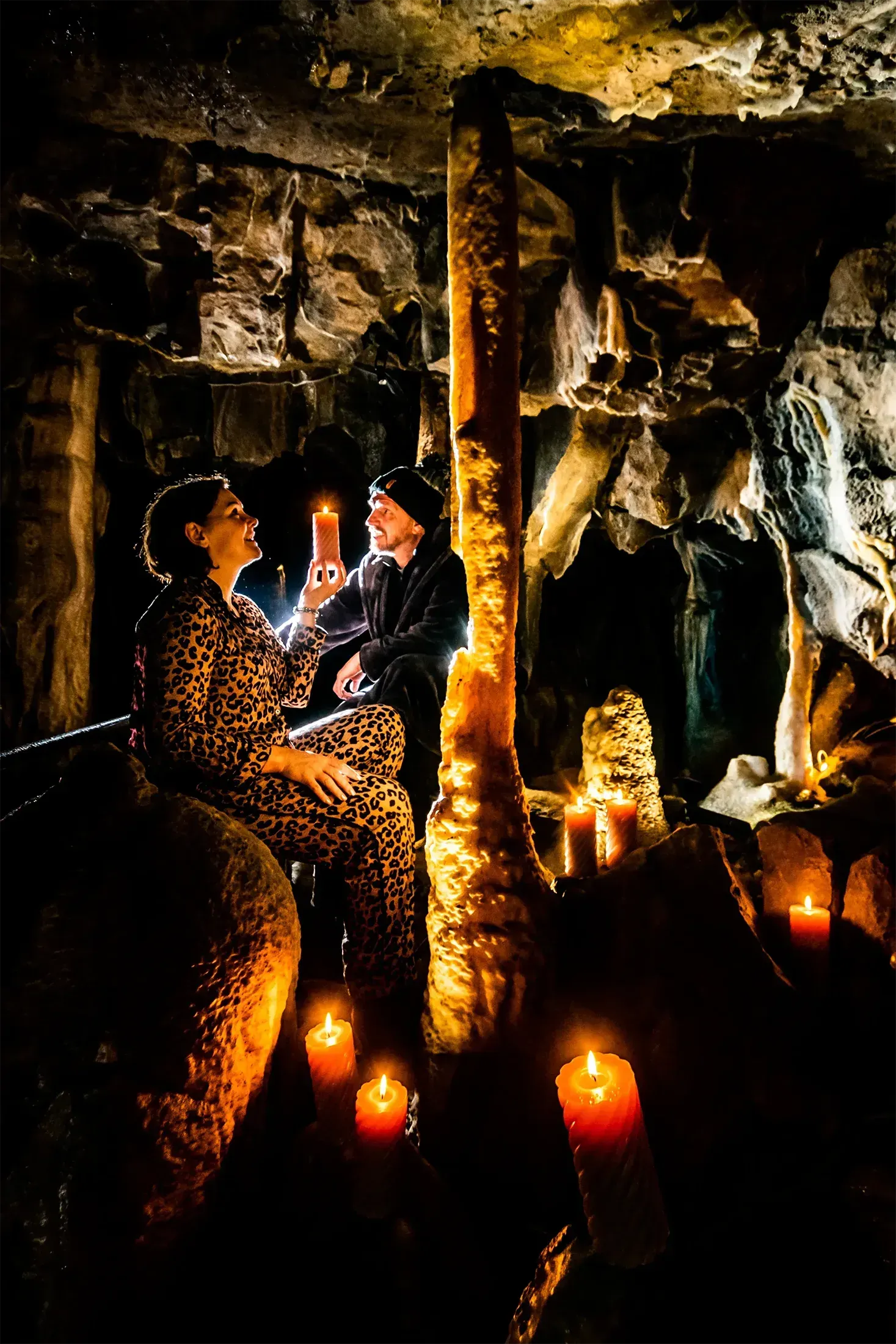 A man and a woman are sitting in a cave surrounded by candles.