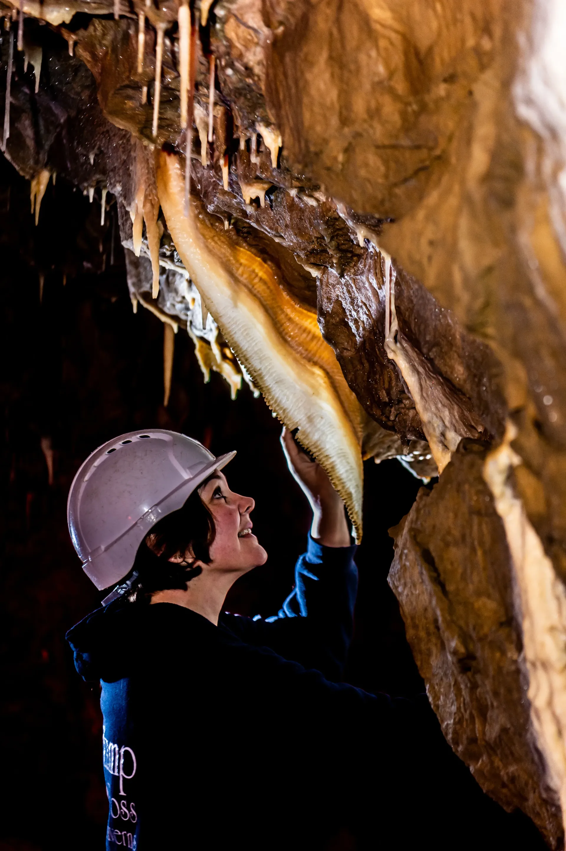 A woman in a hard hat is looking at a rock formation in a cave.