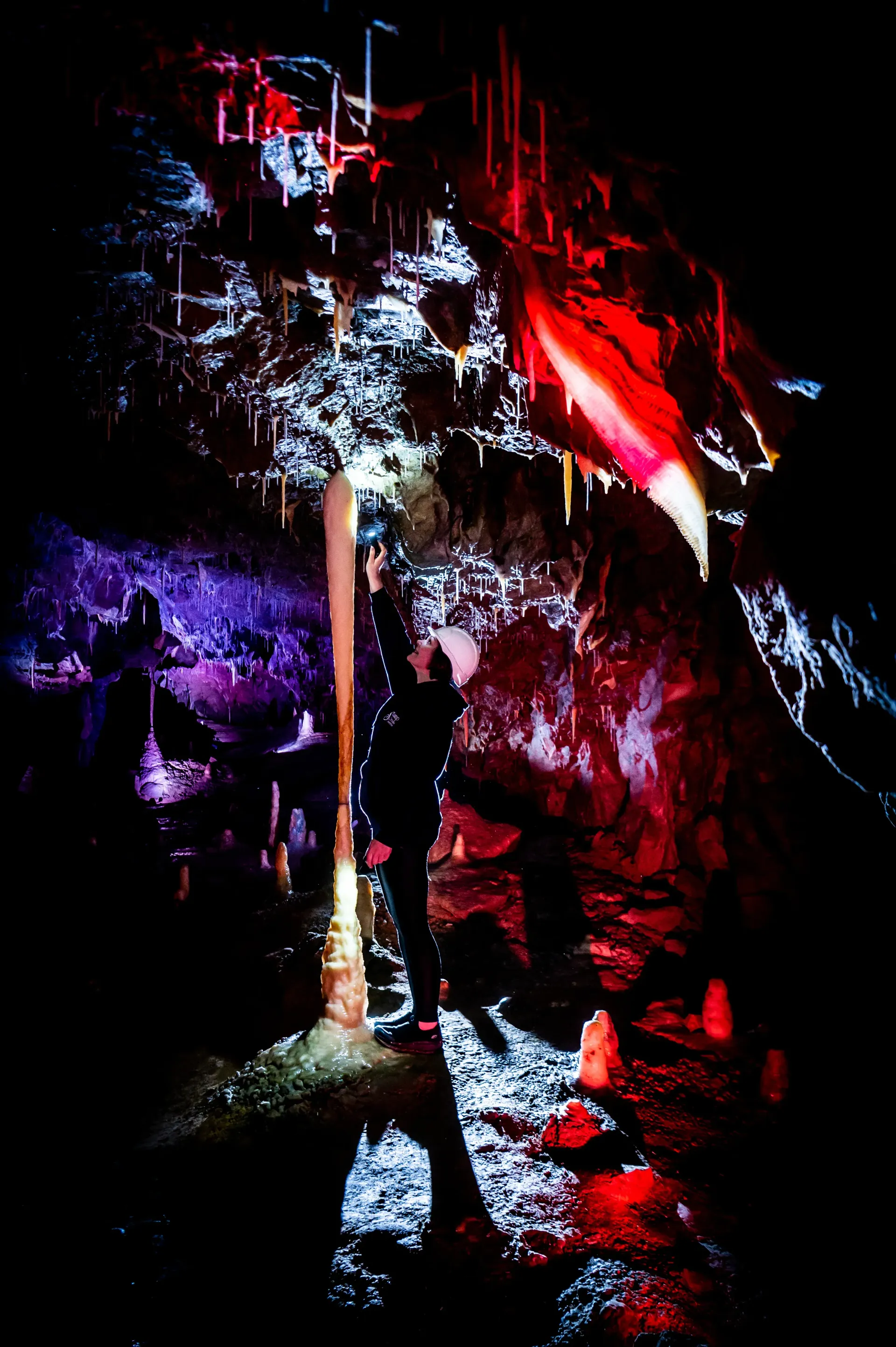 A person is standing in a dark cave with red and purple lights.