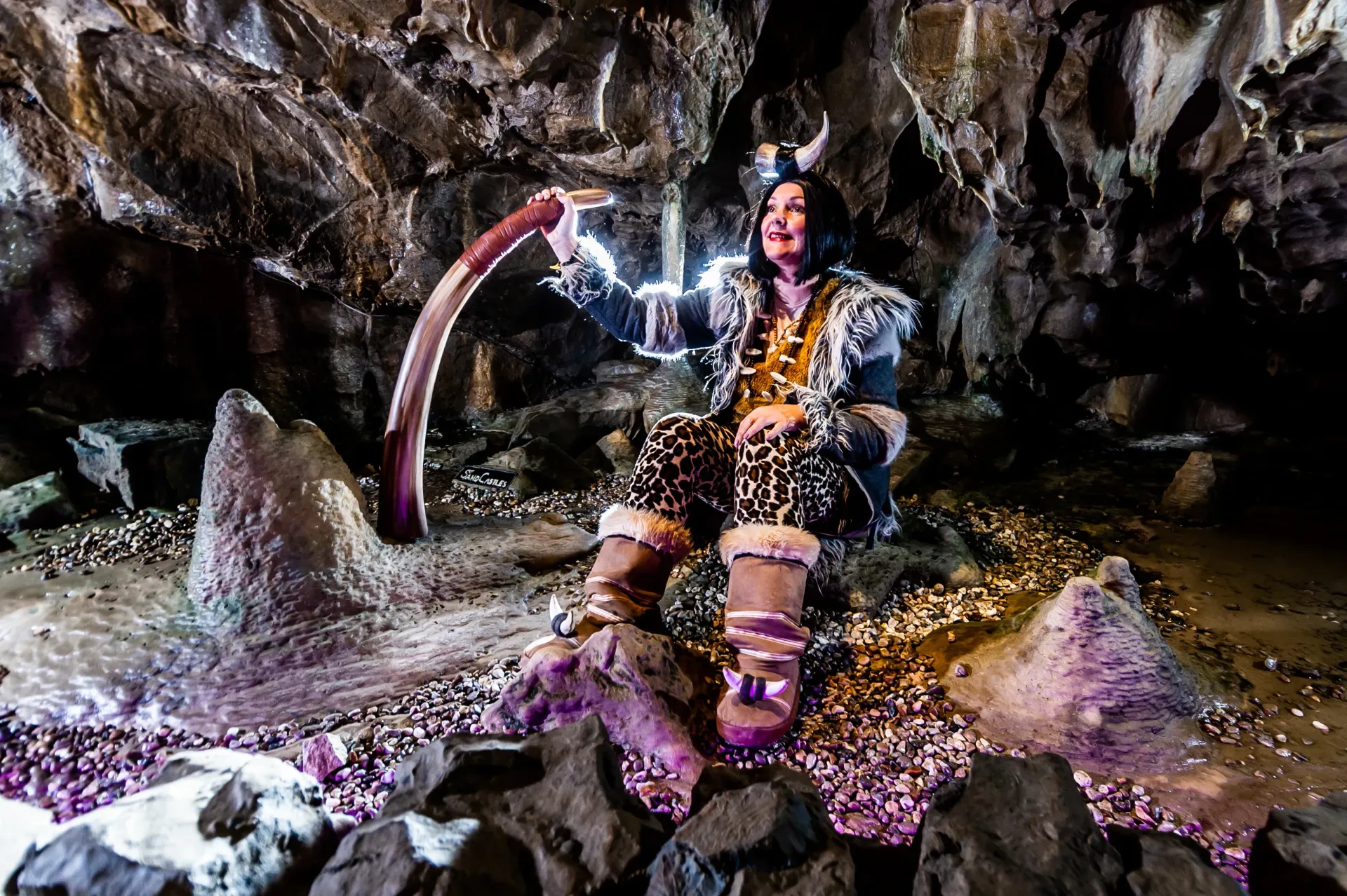 A woman in a costume is sitting in a cave holding a torch.