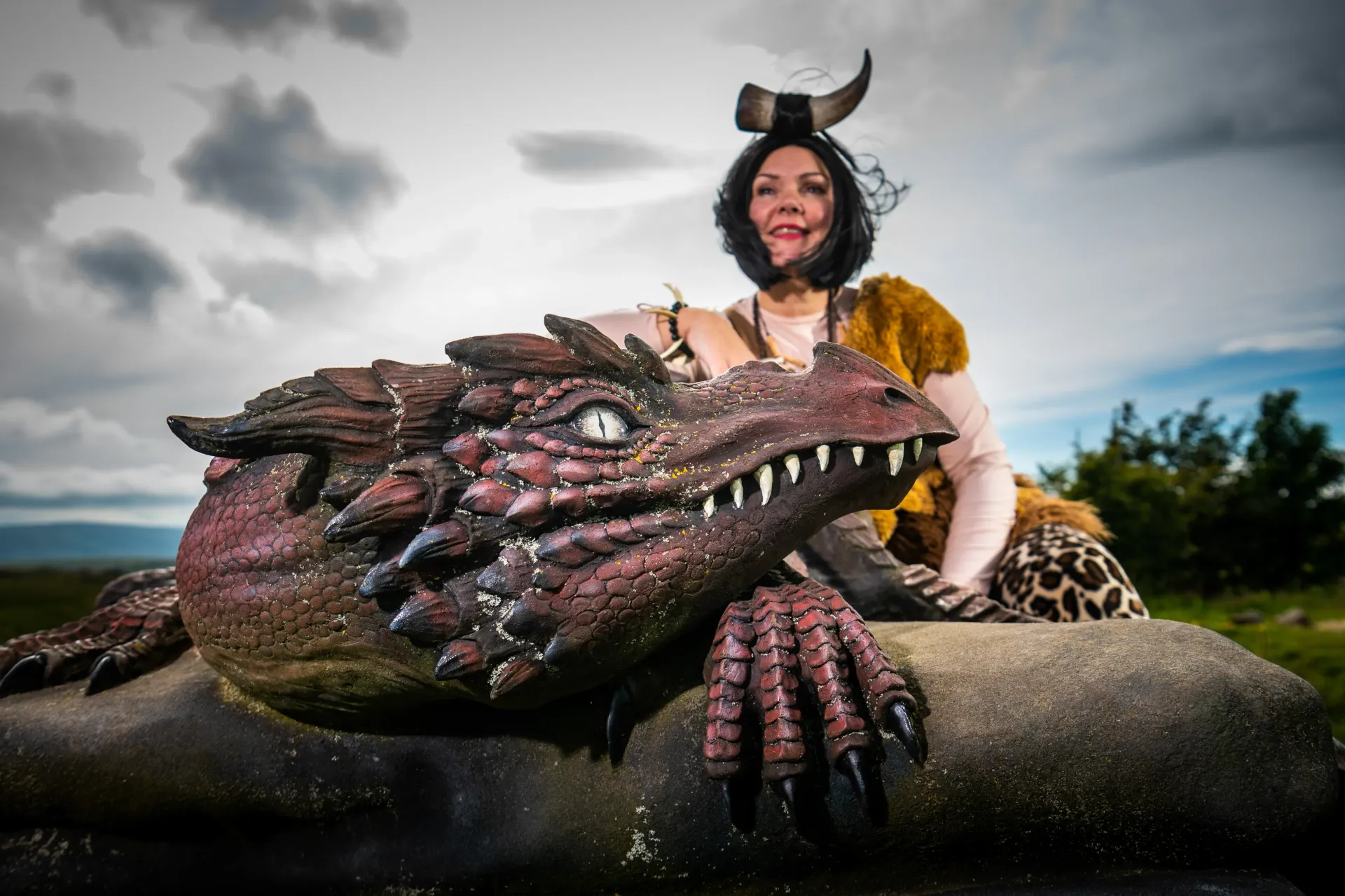 A woman is sitting on a rock next to a dragon statue.